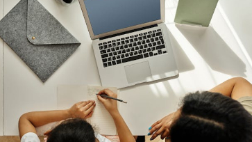 Een volwassene en jongeren zitten samen achter een laptop.