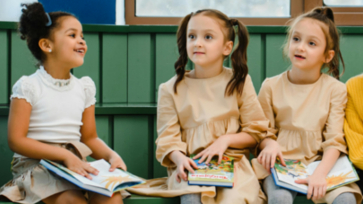 Drie basisschoolleerlingen zitten met een boek op schoot.