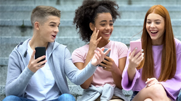 Drie leerlingen in het voortgezet onderwijs lachen samen terwijl ze naar een smartphone kijken.