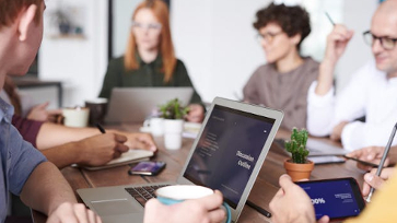 Groep mensen overleggen aan een tafel met laptops op tafel.