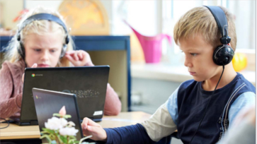Twee leerlingen zitten met koptelefoon op achter laptops in de klas.