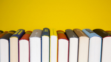 Rij boeken naast elkaar tegen een gele achtergrond.