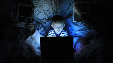 Leerling kijkt in het donker op laptop; het licht van het scherm schijnt op zijn gezicht.