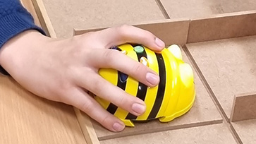 Hand bestuurt een Bee-Bot robot in een houten doolhofbaan