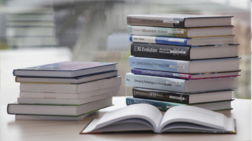 Twee stapels met boeken en een opengeslagen boek.