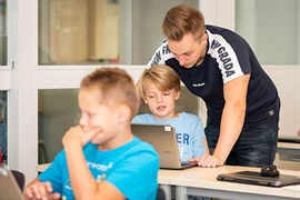 Leraar kijkt mee met leerling op de laptop in de klas.