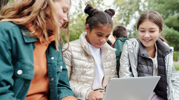 Leerlingen op het schoolplein kijken samen op een laptop.