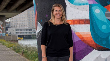 Onderzoeker Esther Rozendaal staat voor een kleurrijke achtergrond onder een brug.