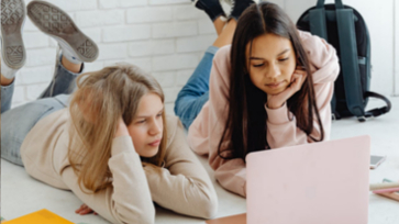 Leerlingen liggen op de grond en kijken samen op een laptop.