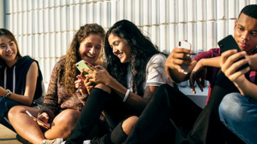 Leerlingen in het voortgezet onderwijs zitten op het schoolplein en kijken samen op smartphone.