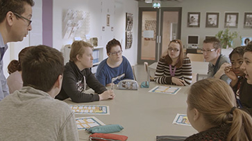 Groep leerlingen zit samen rond een tafel in gesprek.