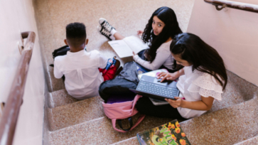 Leerlingen in het voortgezet onderwijs zitten op een trap in school en doen huiswerk